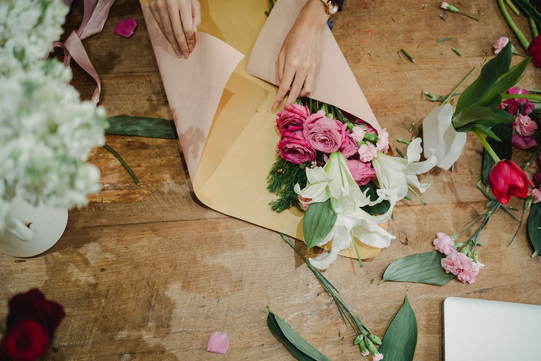 Florist's hands wrapping a fresh bouquet in craft paper on a work bench