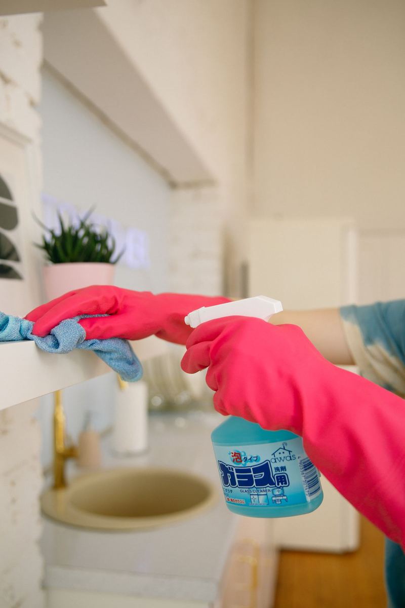 A kitchen shelf being wiped down with a cloth and spray
