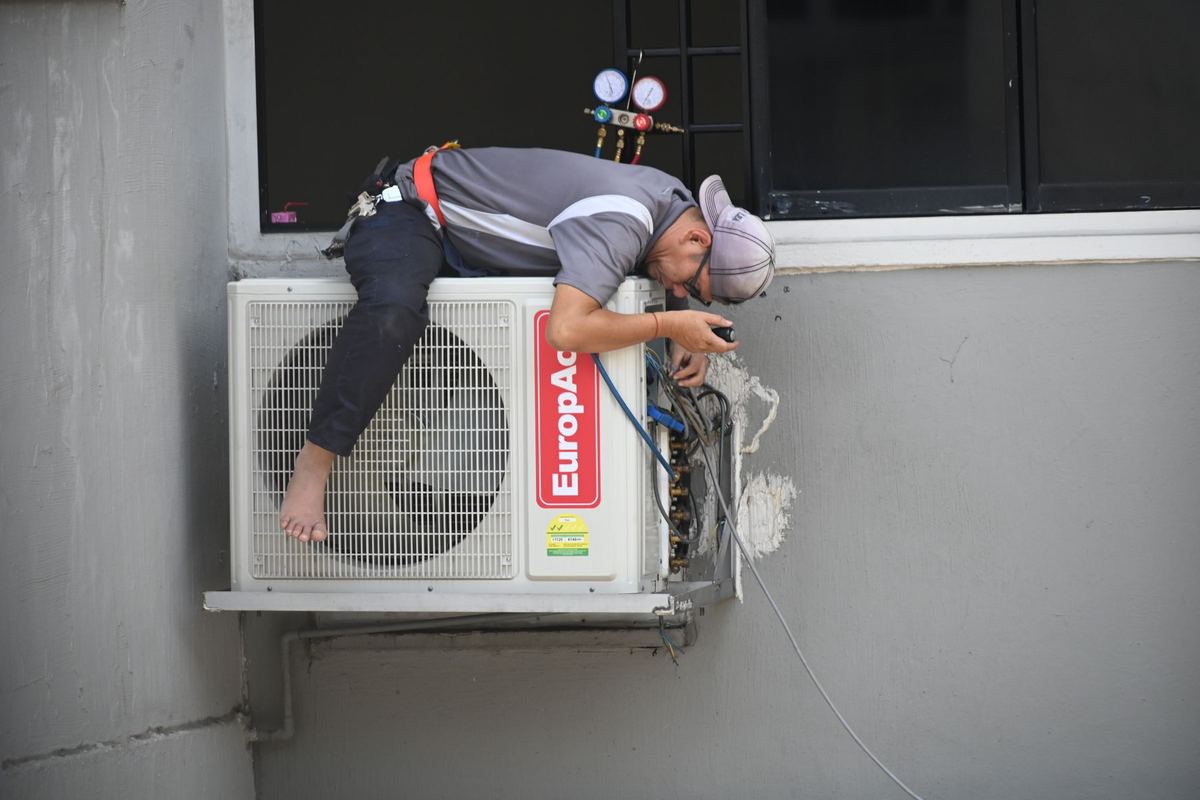 Technician servicing a wall-mounted outdoor condenser unit with refrigerant gauges attached